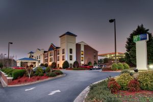 A photograph of the holiday inn express building, and there car park. Green bushes and red flowers can be seen in the photo
